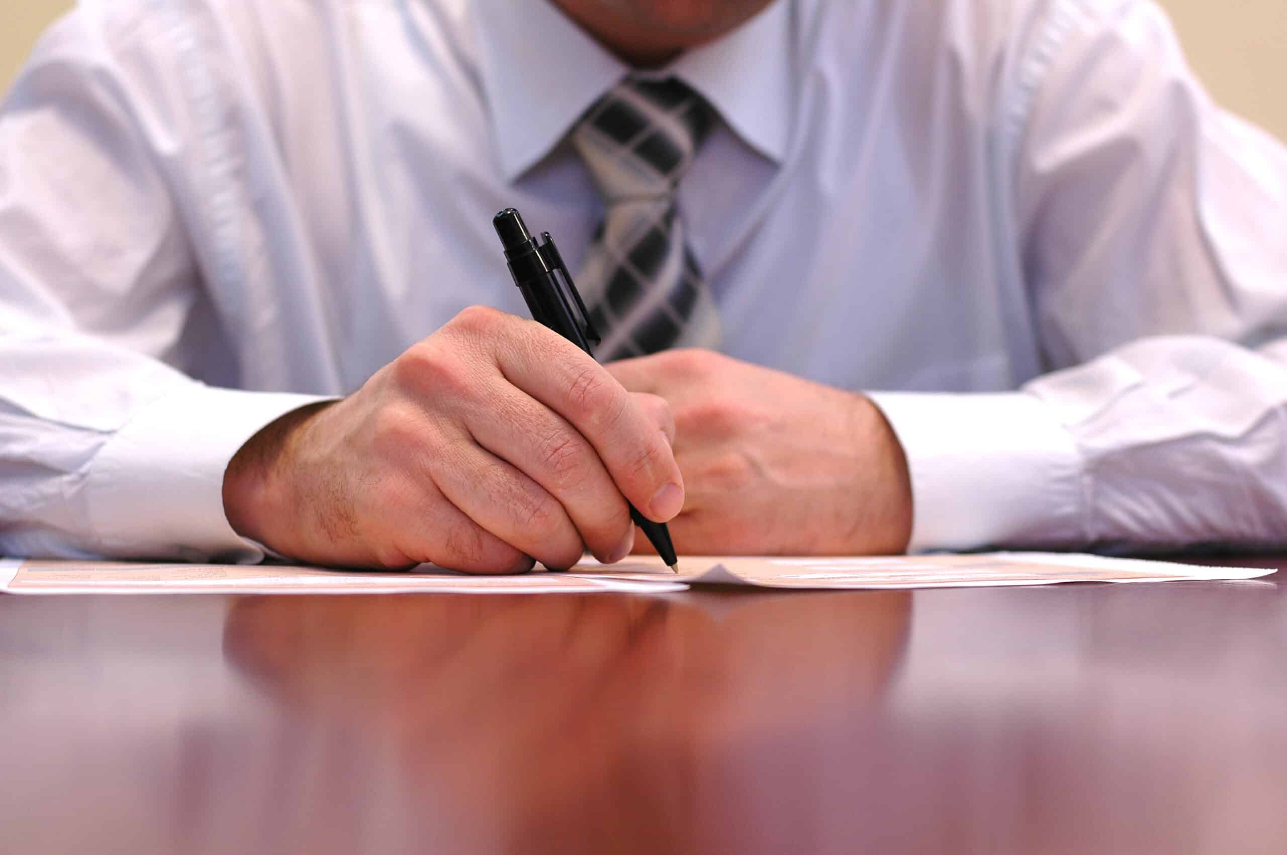 a photo of a man's hands, he is writing on a document on a table